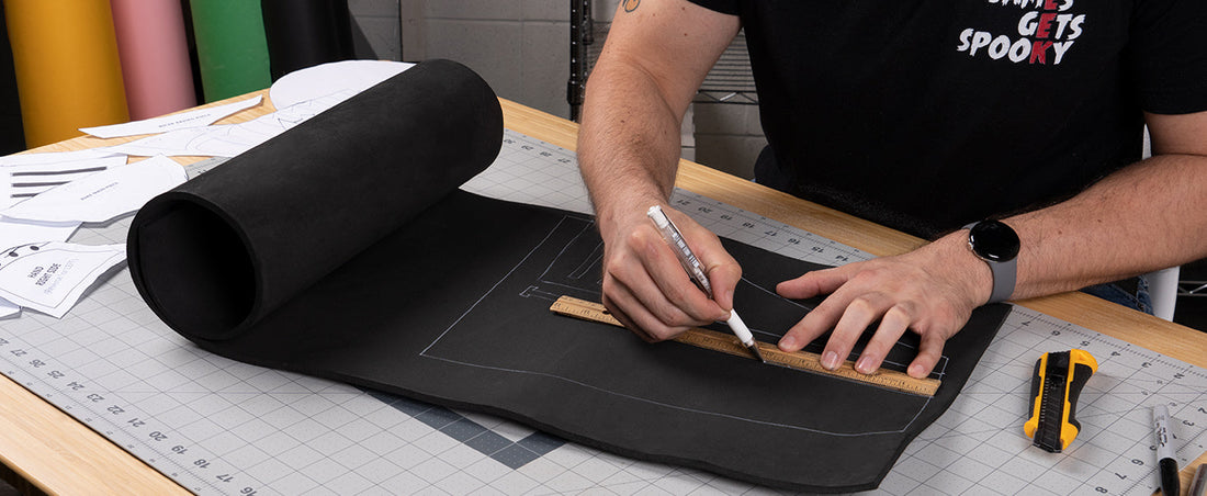 Cosplayer measuring and marking a black EVA foam sheet with a ruler on a cutting mat.