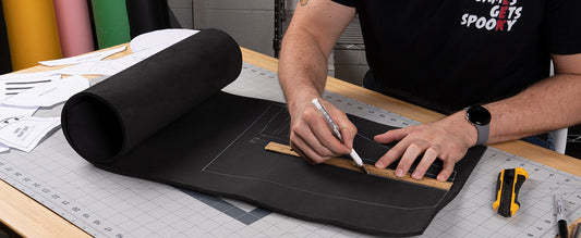 Cosplayer measuring and marking a black EVA foam sheet with a ruler on a cutting mat.